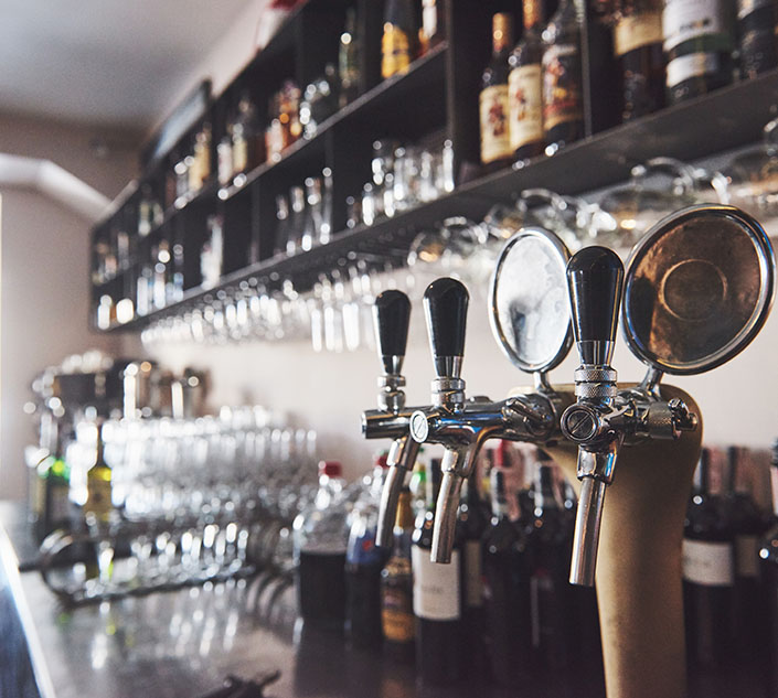 Close-up of beer taps at a bar with shelves filled with various bottles and glassware, showcasing a stylish and vibrant atmosphere.
