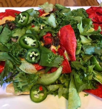 A plate of nachos topped with colorful peppers and fresh green vegetables.