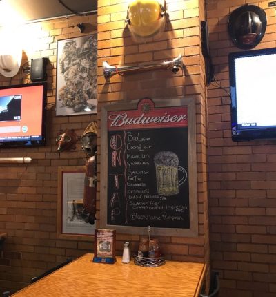 A bar interior featuring a chalkboard menu and a television mounted on the wall.