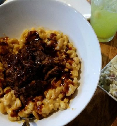 A bowl of macaroni mixed with seasoned ground beef, garnished with melted cheese and herbs.